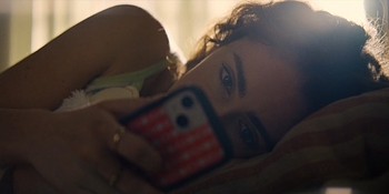 A person lies in bed at golden hour looking at their phone