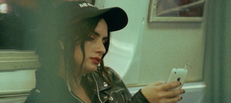 A woman in a black cap and leather jacket looks at her phone on the subway