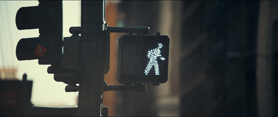 A lit New York crosswalk walk signal glows against a blurred city street