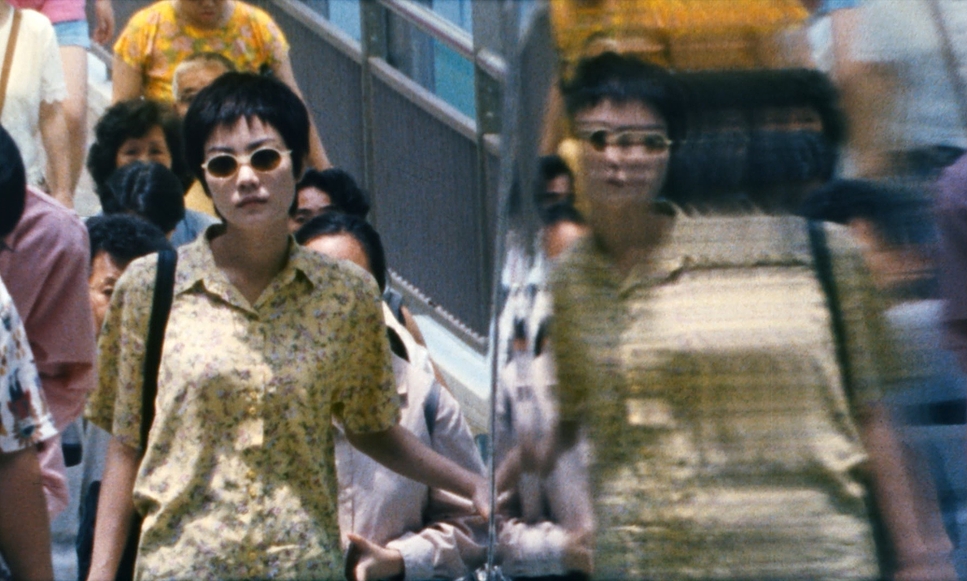 A woman in a crowd mirrored in a reflective surface on a Manhattan street